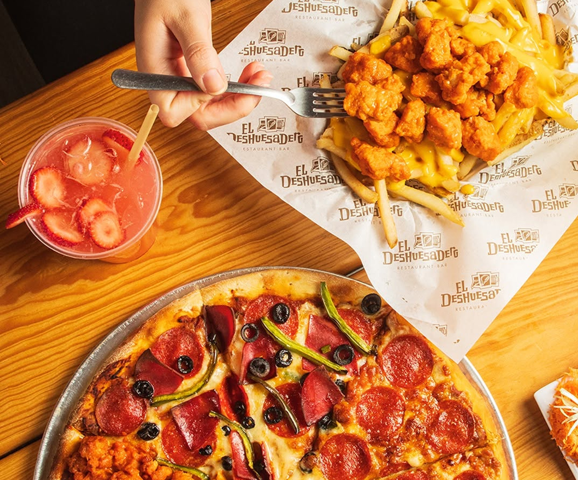 Mesa con pizza de pepperoni, papas con boneless y queso y bebida de fresa
